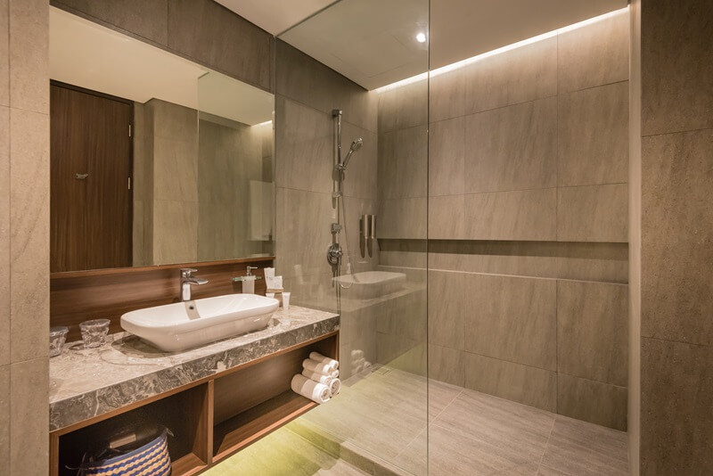 Modern hotel bathroom with a round mirror and walk-in shower