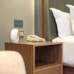 A dark wood bed side table next to a hotel bed