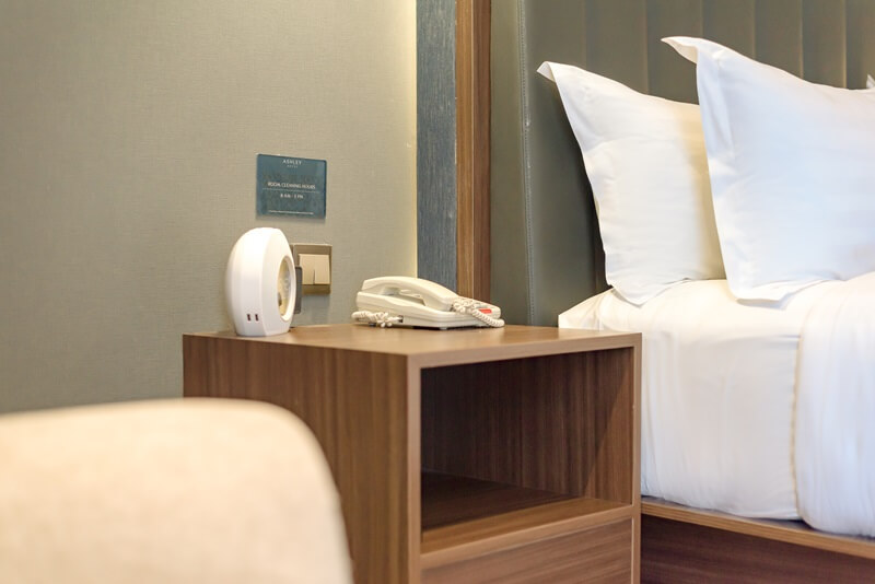 A dark wood bed side table next to a hotel bed