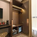 A sunlit hotel room corner with a cozy armchair and lamp