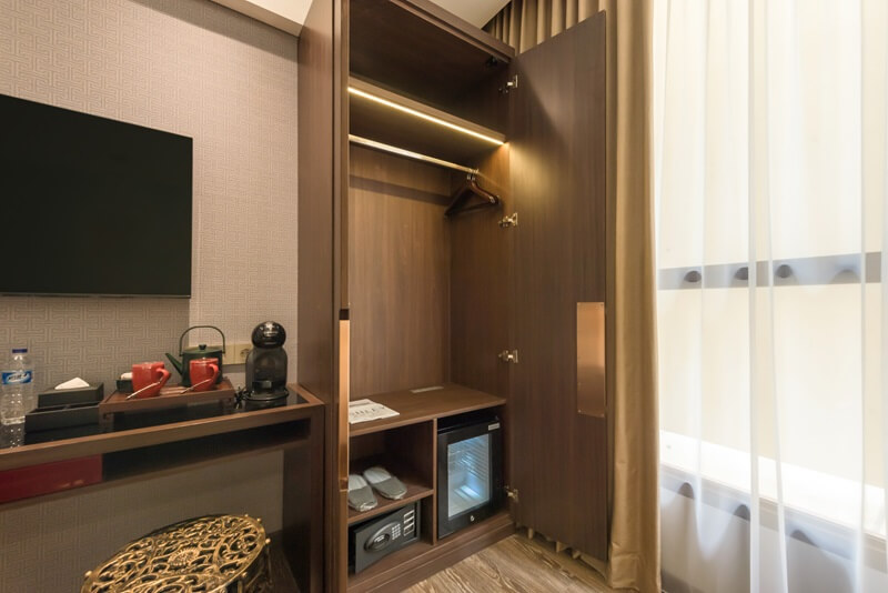 A sunlit hotel room corner with a cozy armchair and lamp